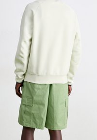 Ljusgröna shorts med sidofickor, tillsammans med en krämfärgad, strukturerad sweatshirt med ribbad nederkant och mudd.
