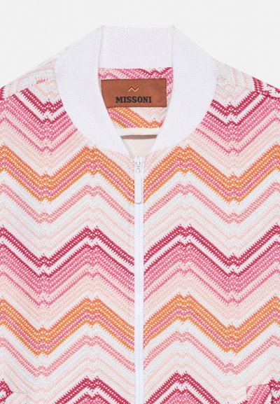 Veste en maille blanche avec des motifs en zigzag rose, rouge et orange, col blanc, fermeture éclair sur le devant et étiquette de la marque Missoni à l’intérieur du col.
