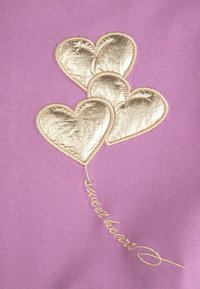 Liliowy materiał ozdobiony jest trzema metalicznymi, złotymi haftowanymi sercami z dekoracyjnym stebnowaniem oraz etykietą z napisem "sweetheart" w stylu pisma ręcznego.