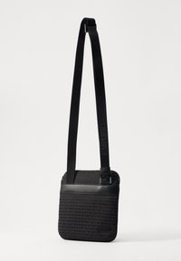 Černá kabelka přes rameno s vzorovanou tkaninou a logem "Emporio Armani" a hladkým koženým akcentem, vybavená nastavitelým popruhem.