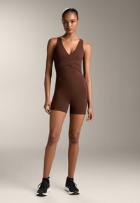 Brun atletisk rompers med V-ringning och korsade detaljer, tillverkad av mjukt, elastiskt tyg. Matchad med svarta träningsskor.