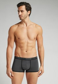 Męskie bokserki w ciemnoszarym kolorze, wykonane z gładkiego materiału. Posiadają czarną elastyczną talię z logo i kontrastującym przeszyciem. Krótki fason nogawki.
