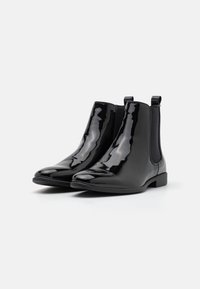 Botas Chelsea de charol negro con paneles elásticos en los costados y tiradores, que presentan un diseño elegante y una forma de punta redondeada. Suelas de goma planas.