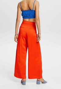 Světlé oranžové kalhoty s širokými nohavicemi a vysokým pasem, s bočními kapsami, v kombinaci s krátkým modrým topem a světlomodrými sandály na podpatku.