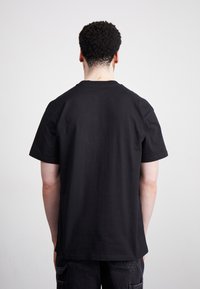 Black cotton t-shirt, short sleeves, standard fit, round neckline, smooth texture, with no visible logos or patterns on the back.
