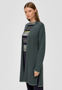 Cardigan long à l'avant ouvert en vert foncé, fabriqué en tissu tricot doux. Présente une bordure arrondie et des coutures contrastées en vert clair.