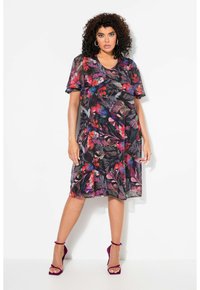 Vestido de flores de manga corta en tela negra transparente, con patrones vibrantes en rojo, rosa y azul, con corte holgado y dobladillo acampanado. Combina con tacones morados.