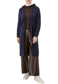 Marineblauer Ripp-Strickcardigan über einem braunen Hoodie, kombiniert mit breiten braunen Lederhosen und cremefarbenen Sneakers. Verfügt über lange Ärmel und eine offene Front.