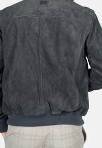 Dunkelgraue Wildleder-Bomberjacke mit geripptem Strickbund. Verfügt über ein einfaches Design und eine strukturierte Oberfläche. Keine sichtbaren Beschläge oder Muster.