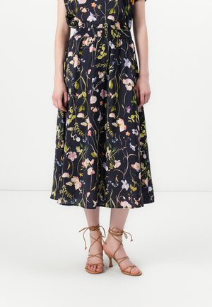 Falda midi floral en navy oscuro, con una cinturilla fruncida y tejido ligero. Combinada con sandalias de tacón alto de tiras en marrón claro.