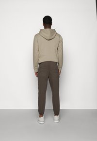 Beżowa bluza z kapturem ze ściągaczem, brązowe spodnie typu cargo i białe trampki; neutralne kolory, casualowy styl i luźny krój.