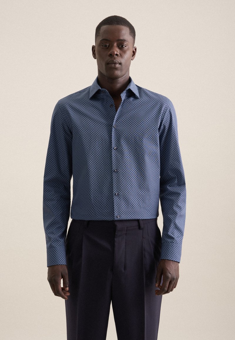 Camicia button-up blu con motivo, colletto strutturato, maniche lunghe e vestibilità slim. Indossata con pantaloni scuri e sartoriali.