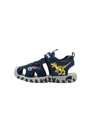 Sandalo per bambini blu navy con grafica di dinosauro, cinturini in velcro, dita aperte e suola grigia robusta progettata per il gioco all'aperto.