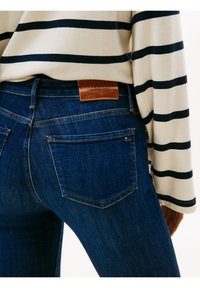 Mörkblå denimjeans med en kroppsnära skärning, med en läderetikett på bakpartiet och diskreta sömmar på fickorna.