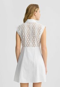 Abito bianco con colletto classico, maniche a cappuccio corte e dettagli in pizzo intagliato intricati sulla schiena. Design della gonna svasata, texture liscia.