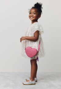 Heart-shaped pink glitter crossbody bag, paired with a sheer white dress adorned with silver star patterns and silver glitter shoes.