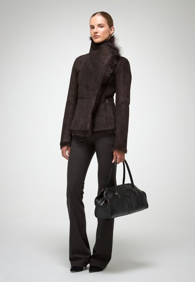 Chaqueta de ante marrón con ribete de piel, diseño entallado, combinada con pantalones gris oscuro y un bolso de cuero negro con asas redondeadas.