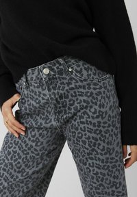 Jean en denim gris à imprimé léopard avec une taille haute, design à cinq poches, et accents de boutons argentés, associé à un pull en tricot noir.