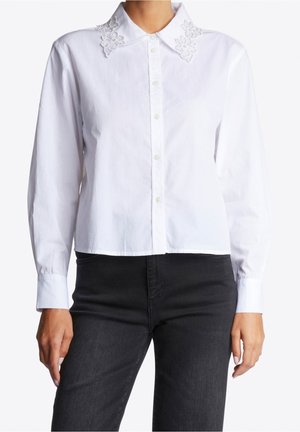 Biała koszula na guziki z długim rękawem, z haftowanym kwiatowym kołnierzykiem, noszona z czarnymi jeansami, widok z przodu od ramion do bioder.