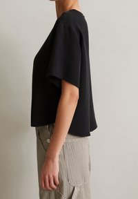 Top nero a maniche corte con vestibilità ampia e scollatura tonda, realizzato in tessuto morbido. Abbinato a pantaloni a righe a vita alta con bottoni.