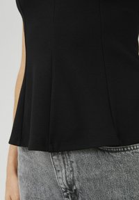 Top noir sans manches avec un ourlet évasé et un buste ajusté. Porté avec un jean taille haute texturé gris. Le tissu semble lisse et extensible.