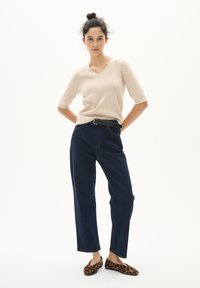 Beige kortärmad V-ringad stickad topp i kombination med högmidjade mörkblå denimjeans. Modellen bär leopardmönstrade slip-on skor.