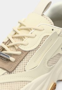 Beige sneaker med mesh och mockamaterial, rund form, gummisulor, tunna snören och en unik överläggsdesign med en texturerad detalj.
