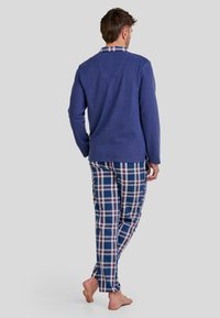 Camiseta de manga larga en color navy combinada con pantalones de lounge de cuadros que presentan líneas azules, rojas y blancas. Tela suave con un corte relajado y cinturilla elástica.