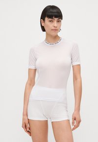 Top bianco in rete a maniche corte con colletto alto e branding a contrasto. Abbinato a pantaloni corti bianchi aderenti, entrambi realizzati in materiale leggero.