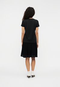 Μαύρο κοντομάνικο μπλουζάκι συνδυασμένο με μαύρη πλισέ φούστα που έχει μεταλλικά τρουκς στη βάση της. Φοράει ψηλοτάκουνα παπούτσια και άσπρες κάλτσες.