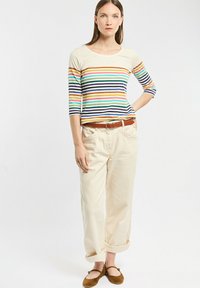T-shirt à manches longues rayé en crème, bleu, orange, vert et bleu marine ; associé à un pantalon beige clair et des ballerines marron. Caractéristiques de coupe décontractée et de poignets retroussés.