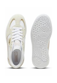Zapatillas PUMA con parte superior de malla blanca y ante beige, cordones planos blancos y suela de goma blanca texturizada con patrones circulares.