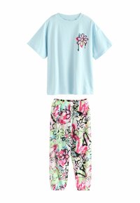 Tricou din bumbac de culoare albastru deschis cu un design floral pe piept. Pantaloni cu elastic și imprimeu floral multicolor pe un fundal deschis.