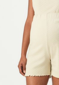 Shorts a maglia beige con vita elasticizzata, caratterizzati da un orlo ondulato e un motivo testurizzato di piccoli punti in rilievo.
