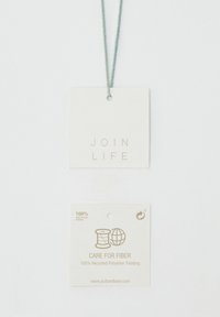 Deux étiquettes blanches pour vêtements suspendues à une corde grise, l'une porte l'inscription "JOIN LIFE,", l'autre "CARE FOR FIBER 100% Recycled Polyester Padding."