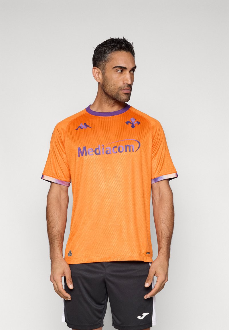 Tricou sport portocaliu din plasă, cu accente mov și logo-ul "Mediacom". Mâneci scurte cu margine albă contrastantă. Pantaloni scurți negri.