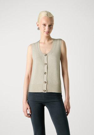 Light beige knit vest with a scoop neckline, button closure, and a ribbed hem. Worn over dark fitted pants.