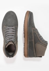 Botas de ante gris a nivel del tobillo con suela de goma marrón en contraste, puntera redonda y seis ojetes para cordones, con costuras dobles y acentos texturizados.