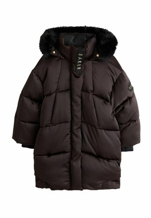 Junge Frau geht und trägt einen langen dunkelbraunen gesteppter Mantel mit Fellkapuze, schwarze Hose und weiße Turnschuhe auf einem grauen Boden.
