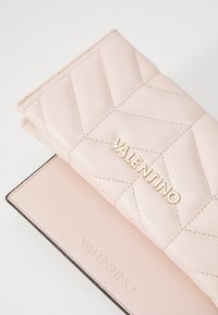 Pokana v roza usnju z zlatim logotipom "VALENTINO" in subtilnim vtisnjenim logotipom na gladki površini.