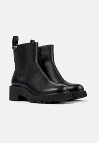 Botas de cuero negro hasta el tobillo con suela de plataforma gruesa, cremallera lateral y tira en el talón. Textura suave y diseño elegante.