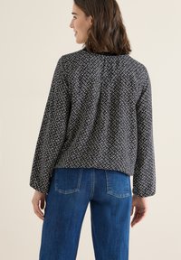 Top a fantasia bianco e nero con maniche lunghe, scollatura rotonda e una vestibilità rilassata, abbinato a jeans in denim blu con tasche posteriori.