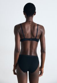 Black lingerie set featuring a smooth fabric bralette with adjustable straps and a matching high-waisted brief, minimalistic design.