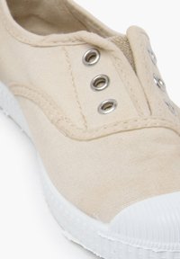 Sneaker in tela beige con suola in gomma bianca, caratterizzata da occhielli in metallo e dettagli di cucitura lungo il bordo del materiale superiore.