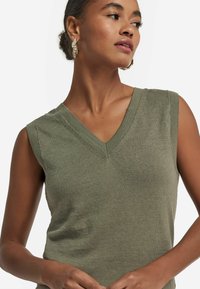 Olivgrön ärmlös topp med V-halsdesign, ribbad textur och en figursydd silhuett. Minimalistisk stil med rena linjer.