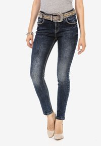 Dunkelblaue Skinny-Jeans mit ausgewaschenen Details, fünf Taschen und einem dekorativen Strassgürtel. Baumwollmischgewebe mit leichtem Stretch.