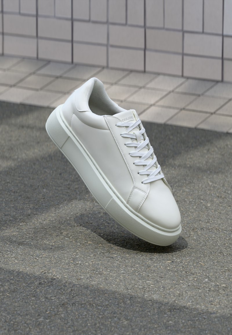 Hvide lædersneakers med en glat overflade, rund tå og flade hvide snørebånd. Har en tekstureret gummisål og minimalt design.