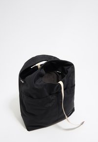 Czarna materiałowa torba z okrągłym otworem, kremowym paskiem i dużą boczną kieszenią. Gładka tekstura i minimalistyczny design.