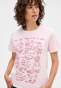 Pink cotton T-shirt featuring playful red illustrations of animals wearing hats, with text caption "They say I wear a lot of hats."