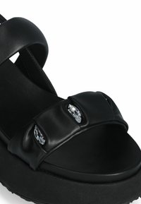 Mustad sandaalid laiade rihmadega, dekoreeritud selgete kristallidega. Pehme nahk ja tekstureeritud must platvormi tall.